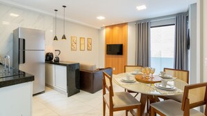 Une cuisine moderne équipée d’un réfrigérateur, d’une cuisinière et d’une machine à café, un coin repas avec une table dressée pour quatre personnes, et un téléviseur fixé au mur.