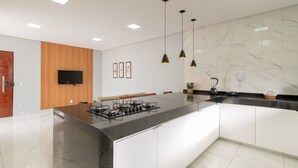 Une cuisine moderne dotée d’un grand îlot central, de meubles blancs, d’un mur d’accent en bois, d’un téléviseur à écran plat, de luminaires suspendus et d’un pare-feu en marbre.