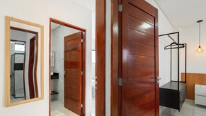 Une pièce avec une porte en bois, un miroir, un luminaire suspendu et un lit blanc.