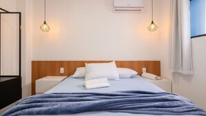 Une chambre d’hôtel comprenant un lit, deux tables de chevet, un appareil de climatisation et deux lampes suspendues.