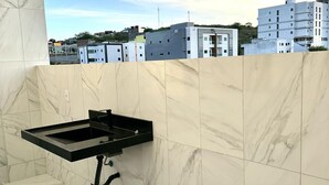 Une salle de bain avec un mur en marbre, un lavabo noir et une vue sur les bâtiments en arrière-plan.