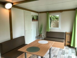 Ein Zimmer mit einem Holztisch, zwei braunen Sofas, einem kleinen Beistelltisch mit einer Pflanze, einer Tür und einem Fenster mit grünen Vorhängen.
