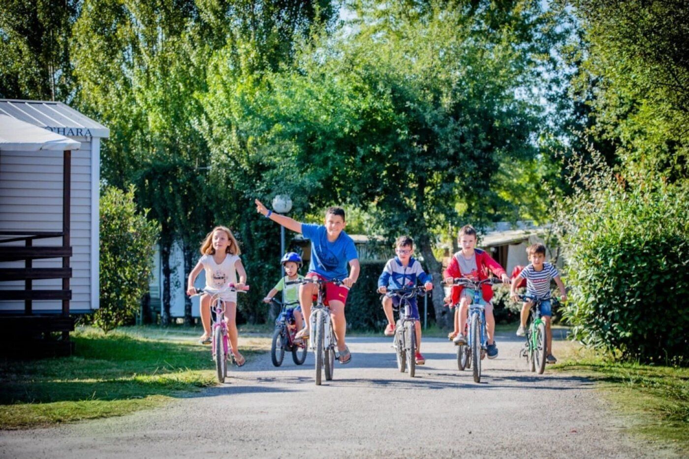 A group of children riding bicycles on a paved path with a mobile home in the background.
