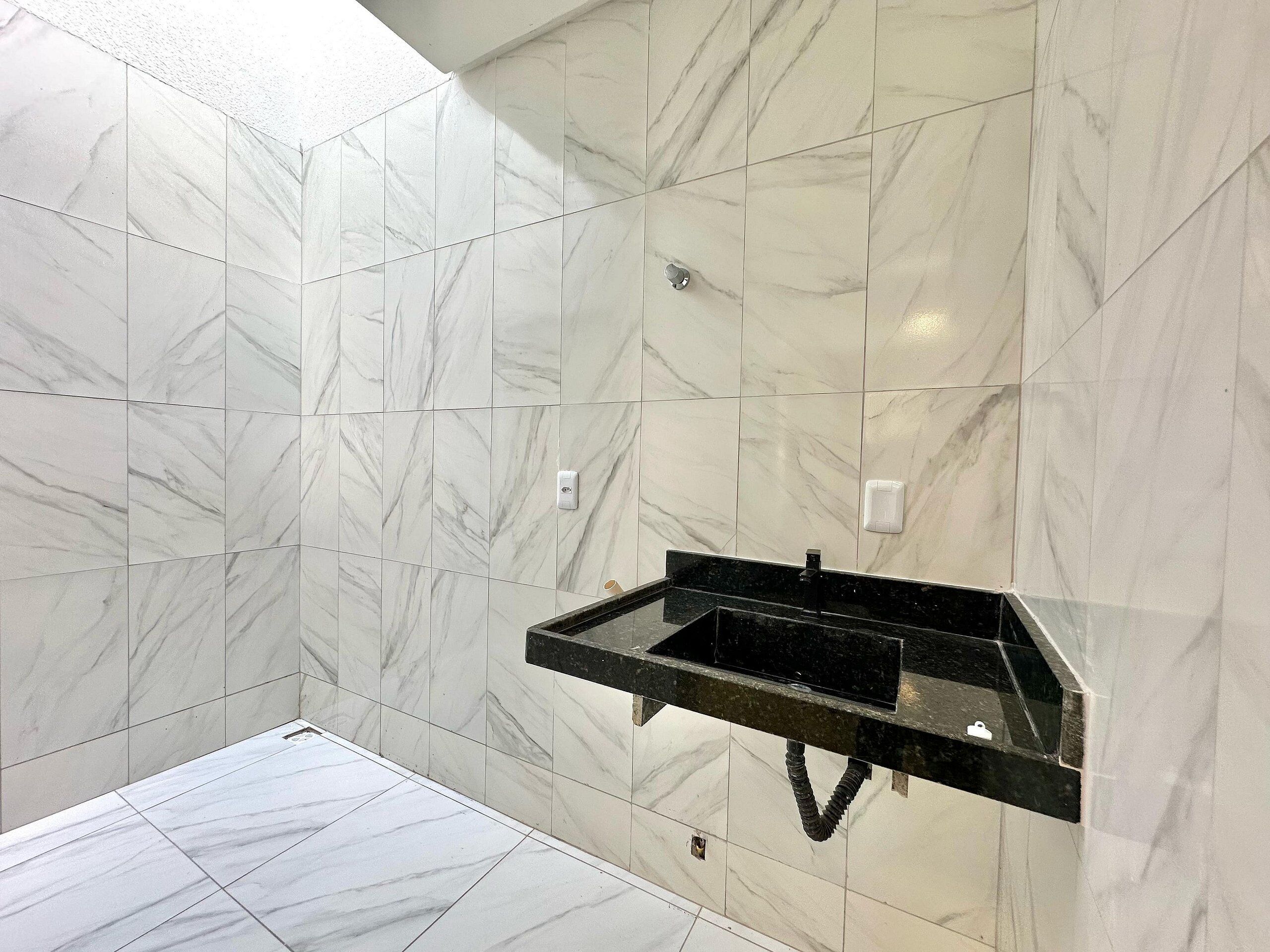Een badkamer met witte marmeren tegels, een zwart wastafelmeubel en een douchehoek.