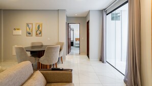 Una sala de estar moderna con una mesa de comedor, sillas y un sofá. Se ve un pasillo que conduce a un balcón con cortinas.