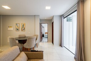 Sala moderna com uma mesa de jantar, cadeiras e um sofá. Há um corredor que leva a uma varanda com cortinas.