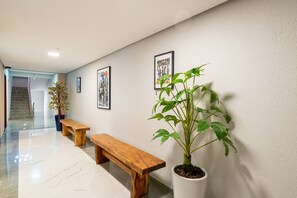 Um corredor com um banco de madeira, uma planta em vaso e quadros nas paredes.