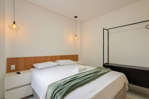 A neatly made bed with a green blanket, a wooden headboard, bedside tables, and a hanging light fixture.