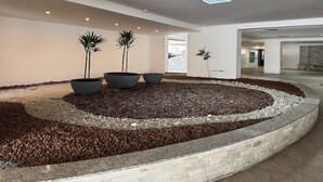 Um jardim interno moderno com três vasos grandes, um leito de pedras e uma parede de pedra curva.