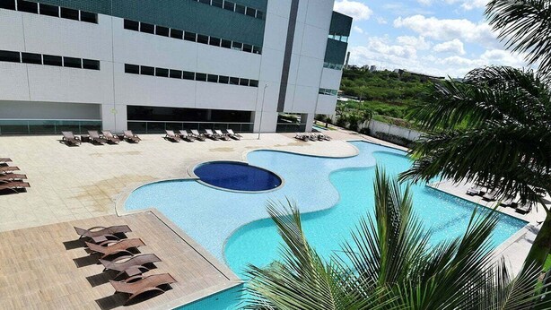 Um hotel moderno com uma grande área de piscina, espreguiçadeiras e palmeiras.