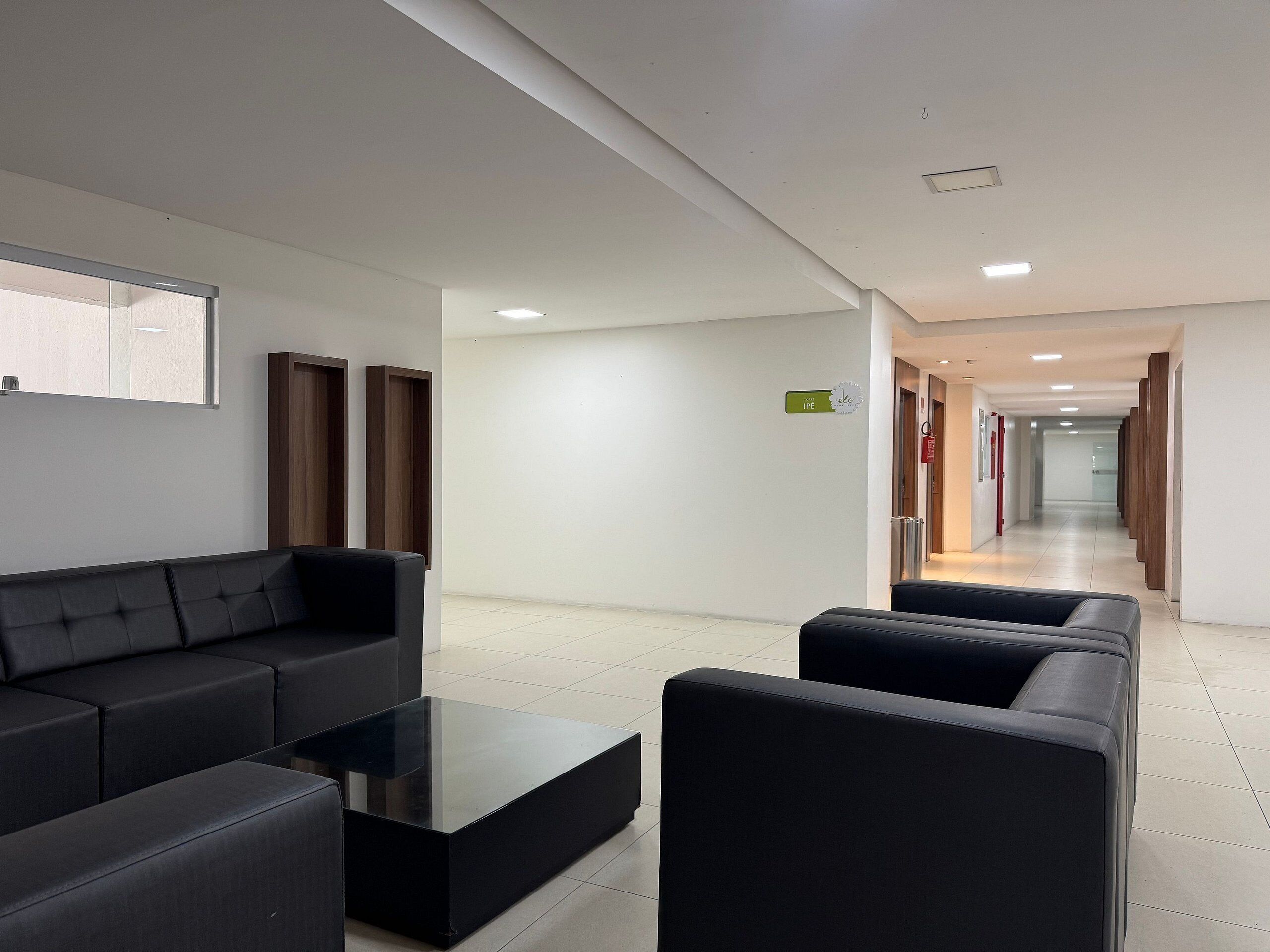 A modern hotel lobby with a black leather sofa, a glass coffee table, and a reception desk.