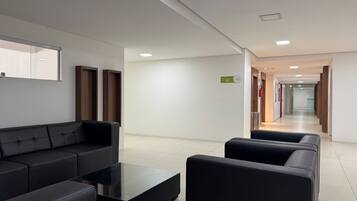 A modern hotel lobby with a black leather sofa, a glass coffee table, and a reception desk.
