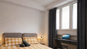 Een hotelkamer met een geruit beddegoed, een bureau met een laptop en een raam met gordijnen.