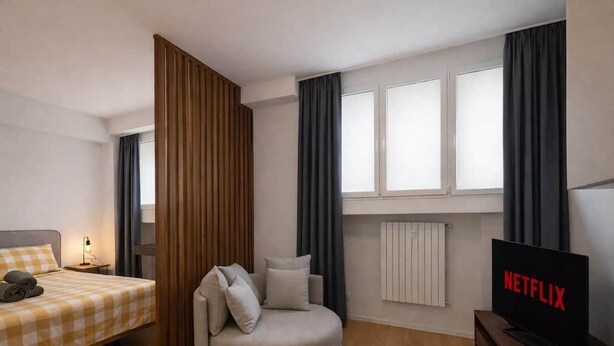 Een moderne hotelkamer met een bed, een bank, een televisie en een raam met gordijnen.