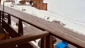 Une terrasse en bois surplombe un paysage enneigé, avec une voiture bleue garée en contrebas.