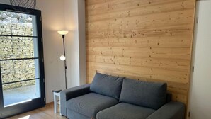 A modern living room with a grey sofa, a small white side table, a floor lamp, and a wooden wall. - 200m from ski slopes, 1st floor, terrace, tv, ski locker, 38m², Saint Gervais (Saint-Gervais-les-Bains)