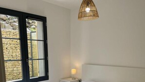 A bedroom with a bed, bedside table, lamp, and a window with a view of a stone wall. - 200m from ski slopes, 1st floor, terrace, tv, ski locker, 38m², Saint Gervais (Saint-Gervais-les-Bains)