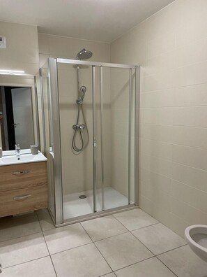 Ein Badezimmer mit Duschkabine, Waschtisch und Spiegel sowie Toilette.