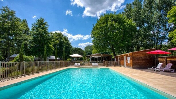 Uma piscina retangular com água azul cristalina, rodeada por um deck de madeira e uma cerca de metal.