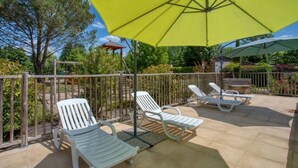 Um pátio externo com cadeiras de lounge brancas e um guarda-sol amarelo.