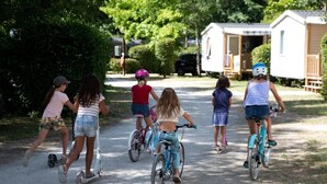 Crianças andando de bicicleta em um caminho de cascalho, com casas móveis ao fundo.