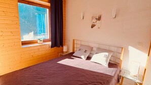 Un dormitorio con una cama grande, paredes de madera, una ventana con cortinas e iluminación montada en la pared.