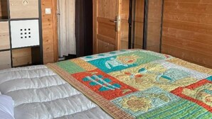 Una stanza di una baita in legno con un letto, una coperta trapuntata, una lampadina, un armadio e un televisore.