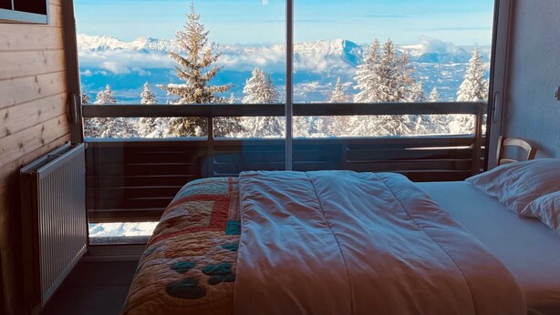 Una camera da letto con una grande finestra, un letto, un termosifone e una lampada a sospensione.