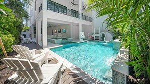 Ein moderner Poolbereich mit Liegestühlen, einer Rutsche und einem zweistöckigen Gebäude mit Balkonen.