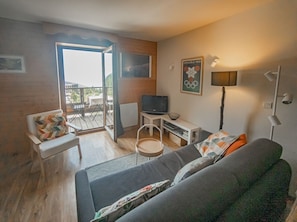 Un salon comprenant un canapé, un téléviseur, une table et une chaise. Il y a un balcon avec vue sur l’extérieur.
