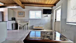 Una cocina compacta con zona de comedor, un televisor montado en la pared y una ventana con persianas.