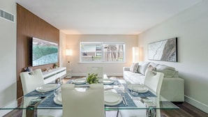 Un comedor moderno con una mesa de vidrio, sillas blancas y vistas al exterior a través de un ventanal.