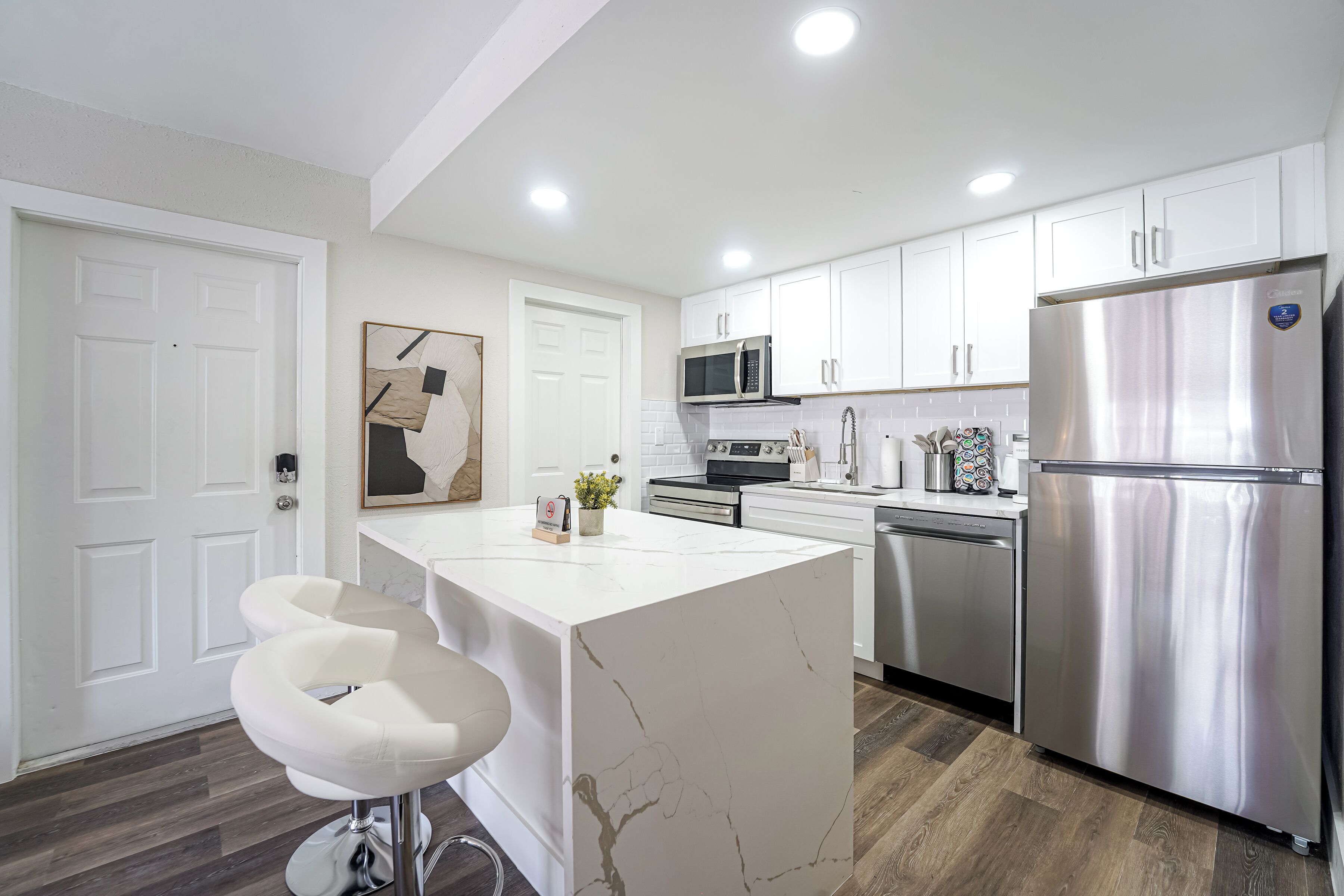A modern kitchen with white cabinets, stainless steel appliances, and a marble island with bar stools.
