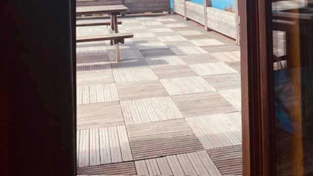 A wooden deck with a checkered floor, a wooden railing, and a view of a body of water and mountains. - Apartment 'Les Edelweiss 201' Large Terrace with Mountain and Valley Views (Chamrousse)