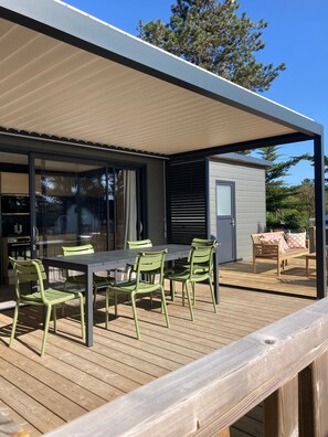 Ein überdachter Essbereich im Freien mit Tisch und Stühlen, eine Terrasse und ein kleines Gebäude mit einem Fenster.