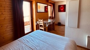 A room with a bed, wooden walls, a dining table with chairs, and a window with curtains. - Studio 'Le Bouquetin 304' for 2 – Les Balcons du Recoin, Chamrousse 1650 (Chamrousse)