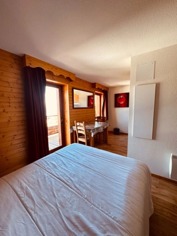 A room with a bed, wooden walls, a dining table with chairs, and a window with curtains. - Studio 'Le Bouquetin 304' for 2 – Les Balcons du Recoin, Chamrousse 1650 (Chamrousse)