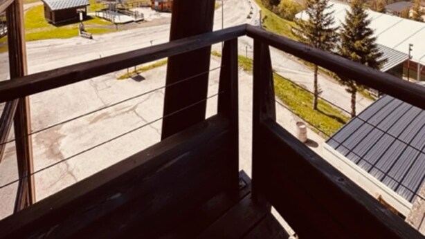 A wooden balcony with a view of a hilly landscape, a road, and a building with a solar panel roof. - Studio 'Le Bouquetin 304' for 2 – Les Balcons du Recoin, Chamrousse 1650 (Chamrousse)