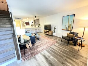 Ein Wohnzimmer mit Sofa, Couchtisch und Fernseher. Eine Treppe führt in einen anderen Raum.