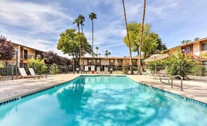 A swimming pool with lounge chairs and palm trees, surrounded by a fence. - Southwest Meets Boho Old Town Scottsdale Townhome (Scottsdale)