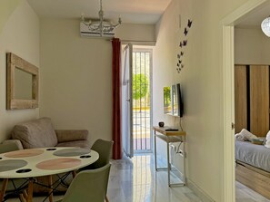 A room with a dining table, chairs, a sofa, a TV, and a bed. - Encanto Alcázar - Ole Solutions (Jerez de la Frontera)