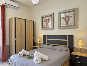 A neatly made bed with towels, a wooden wardrobe, two framed artworks, and bedside lamps. - Encanto Alcázar - Ole Solutions (Jerez de la Frontera)