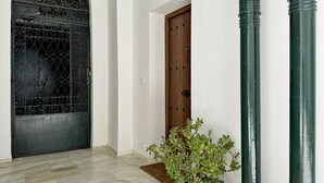 A hallway with a black ornate door, a wooden door, and a potted plant. - Encanto Alcázar - Ole Solutions (Jerez de la Frontera)