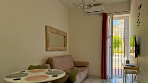 A living room with a sofa, a round table with placemats, a television, and a view through a door. - Encanto Alcázar - Ole Solutions (Jerez de la Frontera)