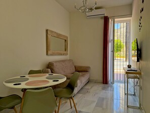 A living room with a sofa, a round table with placemats, a television, and a view through a door. - Encanto Alcázar - Ole Solutions (Jerez de la Frontera)