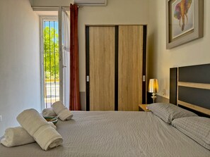 Habitación de hotel con cama, mesita de noche con lámpara, puerta con vistas y un cuadro en la pared.