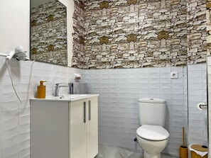 A bathroom with a stone wall, a white sink, a toilet, and a shower area. - Encanto Alcázar - Ole Solutions (Jerez de la Frontera)