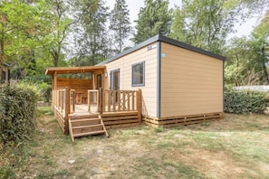 Eine kleine Holzhütte mit Veranda und Tür, umgeben von viel Grün.
