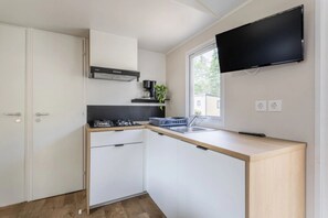 Eine moderne Küche mit weißen Schränken, einer schwarzen Dunstabzugshaube, einem Backofen, einem Spülbecken und einem an der Wand befestigten Flachbildfernseher.