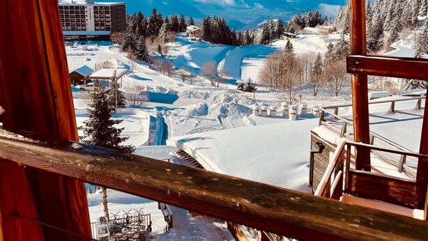 A high-altitude view of a mountainous area with snow-covered terrain, a ski resort, and a building in the distance. - Duplex Apartment 'Les 7 Marmottes', 306, Mountain View and Balcony (Chamrousse)